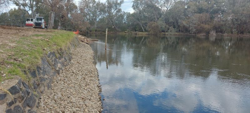 Riverbank with stones and grass, machinery in the backkground