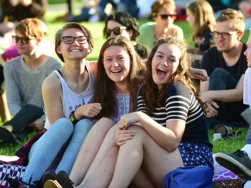 Three young women seated together outdoors, smiling