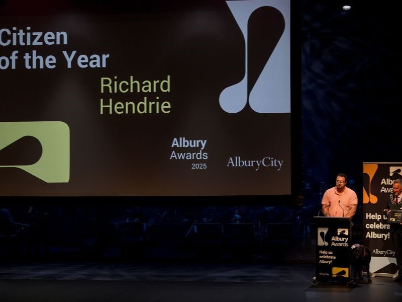 Two men on stage with large screen behind.